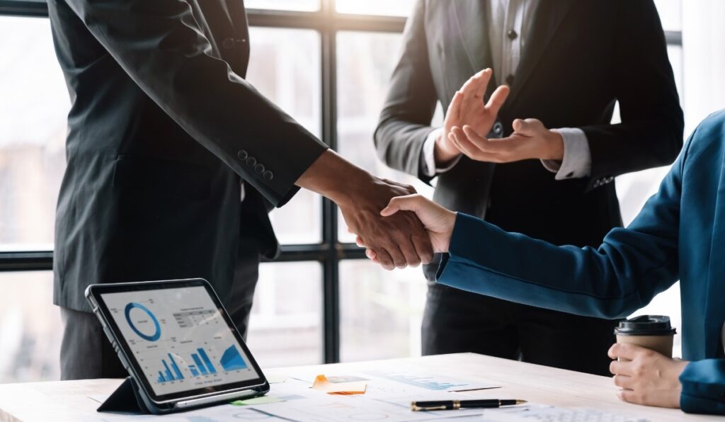 GrantsNow - Ethics and Due Diligence Feature - Image of a business man shaking a clients hand in an office with a laptop on the table